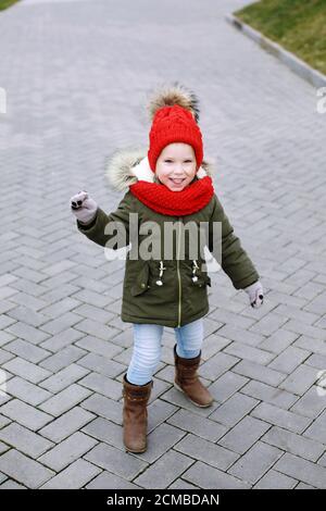 Süße kleine lustige Mädchen in trendigen Outfit Wandern und Tanzen auf der Straße, Spaß haben, winkende Hände, Ganzkörper Blick auf die Kamera Stockfoto