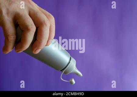 Männliche Hand und graue Plastikflasche mit Sirup. Der Mann hält eine neue Flasche Süßsirup für Eis und Desserts. Selektiver Fokus. Stockfoto