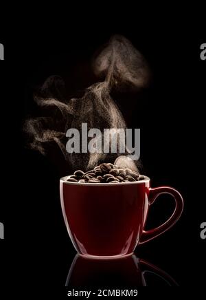 Dampfende rote Tasse gefüllt mit Kaffeebohnen Stockfoto