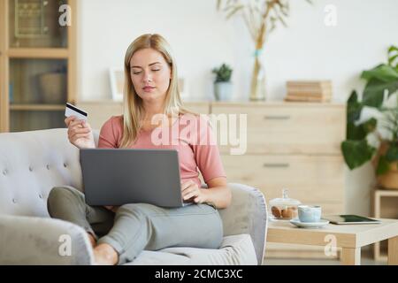 Junge Frau liegt auf dem Sofa mit Laptop und mit Kreditkarte für Online-Shopping zu Hause Stockfoto