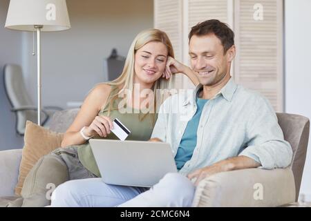 Junges Paar sitzt zusammen auf dem Sofa mit Laptop zu zahlen Online mit Kreditkarte Stockfoto