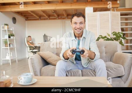 Aufgeregt glücklich Mann sitzt auf dem Sofa mit Joystick und spielen In Computerspielen im Wohnzimmer Stockfoto