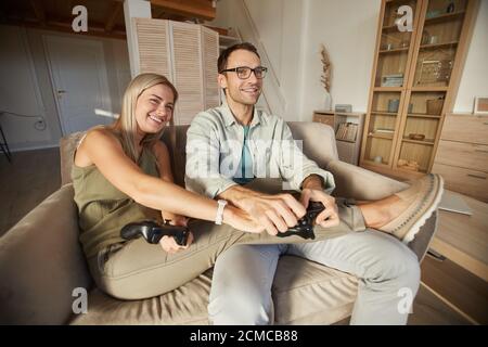 Junges glückliches Paar, das auf dem Sofa sitzt und im Computer spielt Spiele zusammen mit Joysticks zu Hause Stockfoto