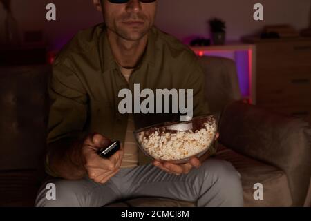 Nahaufnahme eines jungen Mannes, der eine Schüssel mit Popcorn und Fernbedienung hält Steuern und Fernsehen auf dem Sofa zu Hause Stockfoto