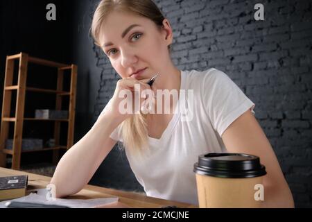 Porträt des SMM-Managers. Junge Frau sitzt hinter dem Schreibtisch mit Stift in der Hand und Papier-Kaffeetasse Stockfoto