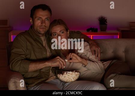 Junges Paar, das sehr erschrocken aussieht, liegen sie auf dem Sofa mit Popcorn und schaue einen gruseligen Film Stockfoto