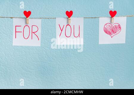 Rote Valentine's Love Hearts Pins hängen auf natürliche Schnur auf blauem Hintergrund. Für Sie handgeschriebener Text auf Papierstücken. Stockfoto