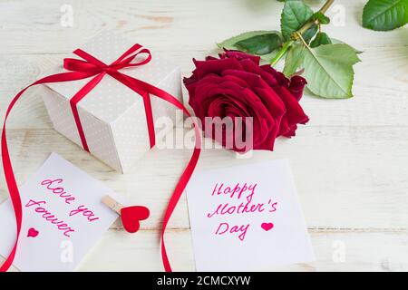 Beigefarbene Geschenkschachtel mit roter Schleife und schönen roten Rosen auf Holzhintergrund. Grußkarte zum Muttertag Stockfoto