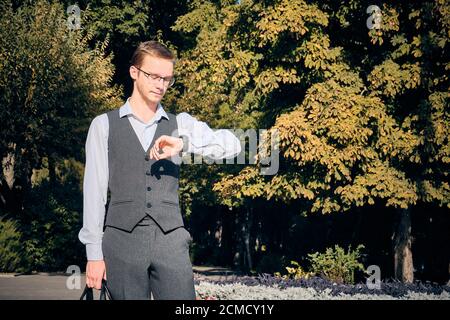 Junger Mann in weißem Hemd und Weste sieht an Die Uhren am Handgelenk Stockfoto