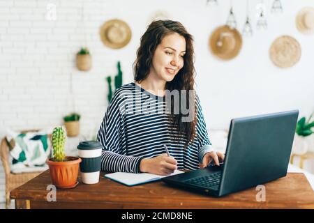 Positive hübsche Frau mit langen Haaren zu Hause im Büro am Schreibtisch arbeitet. Stockfoto