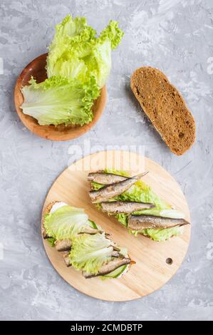 Sprotte Sandwiches mit Salat und Frischkäse auf Holzbrett auf grauem Beton Hintergrund. Draufsicht, flach liegend. Stockfoto