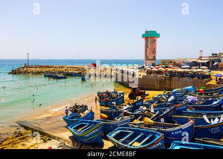 Agadir, Marokko - 14. AUGUST 2020 : der Hafen von Imesouane. Blaue Boote, Möwen, ein Traktor, Kaffee, Fischer, Menschen schwimmen und ein Kontrollturm Stockfoto