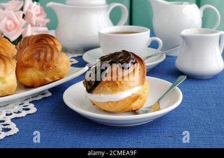 Eclair mit Schokoladenfrosting auf einem Teller mit einer Tasse Kaffee Stockfoto