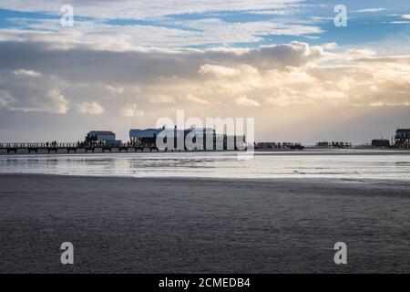 Panoramablick auf Stelzenhäuser und hölzernen seabridge bei Ebbe Nordseestrand bei Sonnenuntergang in Sankt Peter-Ording, Deutschland gegen dramatischen Himmel Stockfoto