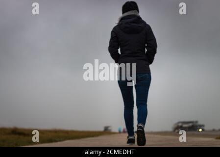 Low-Angle-Ansicht der unkenntlich verschwommenen Frau zu Fuß weg auf Ein hölzerner Fußweg am Nordseestrand Stockfoto