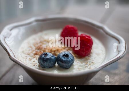 Nahaufnahme von Haferbrei in einer Schüssel mit Heidelbeeren und Himbeeren Auf einem Holzbrett Stockfoto