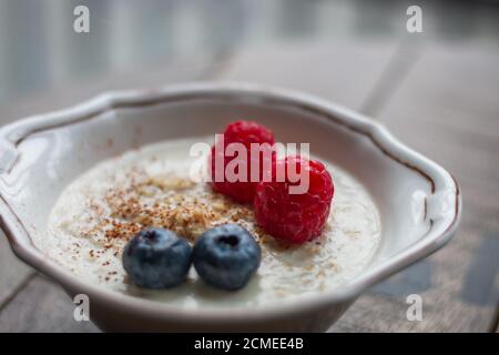 Nahaufnahme von Haferbrei in einer Schüssel mit Heidelbeeren und Himbeeren Auf einem Holzbrett Stockfoto