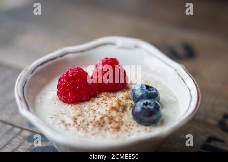 Nahaufnahme von Haferbrei in einer Schüssel mit Heidelbeeren und Himbeeren Auf einem Holzbrett Stockfoto