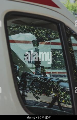 Vertikale Aufnahme eines Innenraums eines Krankenwagens in Split, Kroatien. Parken auf dem öffentlichen Parkplatz, Spiegelung der Bäume auf dem Fenster. Facemask hängen Stockfoto