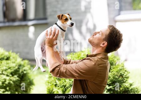 Junger Mann, der draußen steht und Jack russell Terrier Hund aufzieht Auf Händen Stockfoto