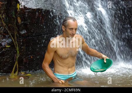 Glücklicher Mann, Prospektor, der Gold in einen Fluss mit Schleusenkasten schwenkt Stockfoto