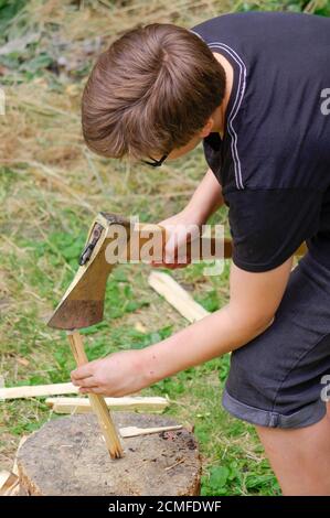 Kleiner Junge, der eine Axt in der Hand auf einem hält Hintergrund des dichten Waldes Stockfoto