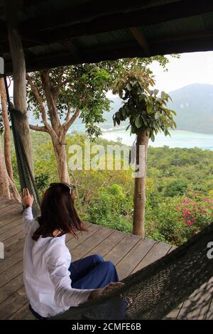 Lässige glückliche Frau, die sich in einer Hängematte mit Meerblick vom Aussichtspunkt, Krabbi Island, Thailand, entspannt Stockfoto