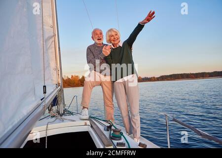 Aufgeregt Senior Paar Hände halten und lächeln, während auf der Seite der Yacht Deck schwimmend im Meer, Frau zeigt auf den Horizont, Segeln Stockfoto
