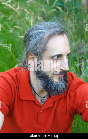 Junge bärtige Mann sitzt drausen auf sonnigen Tag mit grünem Hintergrund. Dies ist ein Porträt Stockfoto