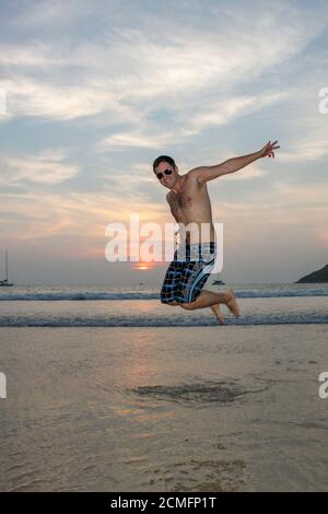 Mann springt glücklich am Strand mit Sonnenuntergang Himmel in Der Hintergrund Stockfoto