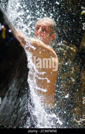 Mann, der eine entspannende Dusche unter einem Wasserfall. außerhalb Stockfoto