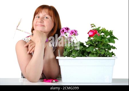 Porträt einer hübschen Frau mittleren Alters mit Pelargonien in einem Blumentopf. Stockfoto