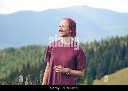 Mädchen mit rosa Haaren auf der Lichtung stehen und schaut auf die Berge. Wandern durch den Wald im Sommer. Dunkler Herbstwald. Lokales Reisekonzept Stockfoto