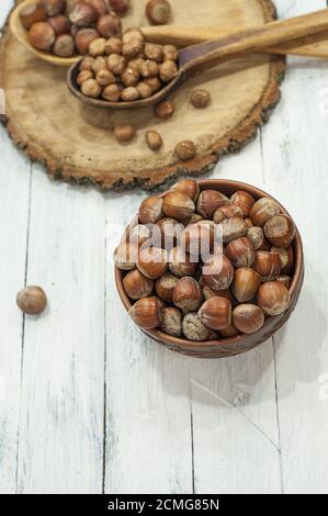 Haselnüsse in Schale in brauner Tonschale auf einem weißen Holzhintergrund Stockfoto