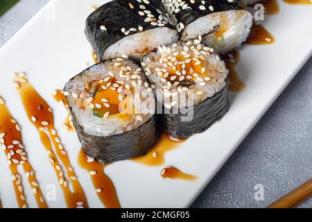 Sushi setzt Nigiri, Uramaki, California, Philadelphia, auf einen weißen Teller. In der Nähe Ingwer und Wasabi. Sojasauce in einer weißen Schüssel. Auf hellgrauem Hintergrund Stockfoto