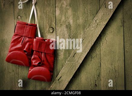 Rote Leder Boxhandschuhe hängen an einem Nagel in der Holzwand Stockfoto