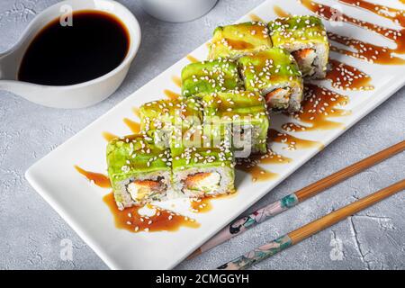 Sushi setzt Nigiri, Uramaki, California, Philadelphia, auf einen weißen Teller. In der Nähe Ingwer und Wasabi. Sojasauce in einer weißen Schüssel. Auf hellgrauem Hintergrund Stockfoto