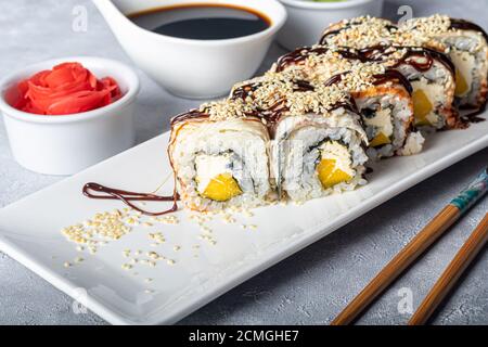 Sushi setzt Nigiri, Uramaki, California, Philadelphia, auf einen weißen Teller. In der Nähe Ingwer und Wasabi. Sojasauce in einer weißen Schüssel. Auf hellgrauem Hintergrund Stockfoto