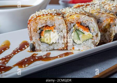 Sushi setzt Nigiri, Uramaki, California, Philadelphia, auf einen weißen Teller. In der Nähe Ingwer und Wasabi. Sojasauce in einer weißen Schüssel. Auf hellgrauem Hintergrund Stockfoto