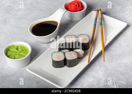 Sushi setzt Nigiri, Uramaki, California, Philadelphia, auf einen weißen Teller. In der Nähe Ingwer und Wasabi. Sojasauce in einer weißen Schüssel. Auf hellgrauem Hintergrund Stockfoto