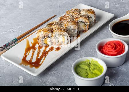 Sushi setzt Nigiri, Uramaki, California, Philadelphia, auf einen weißen Teller. In der Nähe Ingwer und Wasabi. Sojasauce in einer weißen Schüssel. Auf hellgrauem Hintergrund Stockfoto
