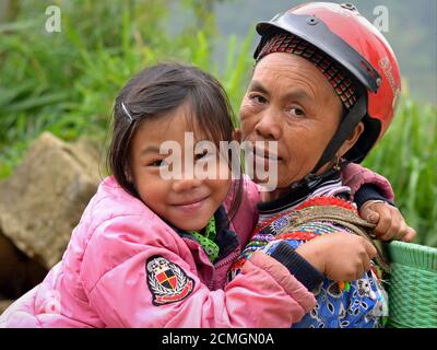 Ältere Vietnamesin Hmong ethnische Minderheit Hügel-Stamm Frau mit Sturzhelm hält ihre niedliche kleine Enkelin in den Armen und posiert für die Kamera. Stockfoto