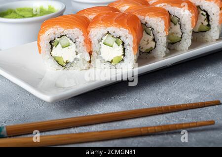 Sushi setzt Nigiri, Uramaki, California, Philadelphia, auf einen weißen Teller. In der Nähe Ingwer und Wasabi. Sojasauce in einer weißen Schüssel. Auf hellgrauem Hintergrund Stockfoto
