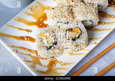 Sushi setzt Nigiri, Uramaki, California, Philadelphia, auf einen weißen Teller. In der Nähe Ingwer und Wasabi. Sojasauce in einer weißen Schüssel. Auf hellgrauem Hintergrund Stockfoto