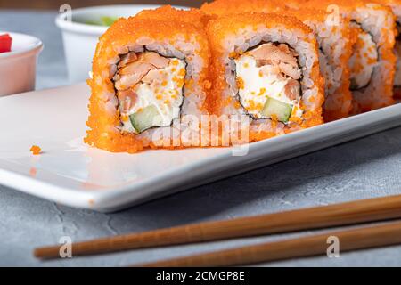 Sushi setzt Nigiri, Uramaki, California, Philadelphia, auf einen weißen Teller. In der Nähe Ingwer und Wasabi. Sojasauce in einer weißen Schüssel. Auf hellgrauem Hintergrund Stockfoto