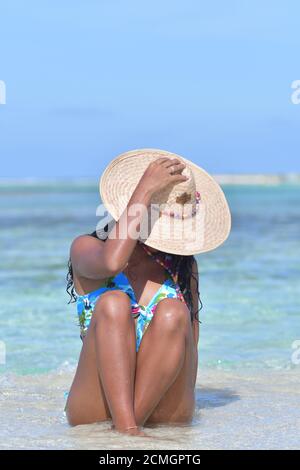 Hispanische Frau sitzt am Sandstrand und lacht mit geschlossenen Augen und Spritzwasser. Los Roques Venezuela Stockfoto