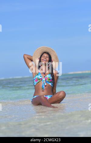 Hispanische Frau sitzt am Sandstrand und lacht mit geschlossenen Augen und Spritzwasser. Los Roques Venezuela Stockfoto