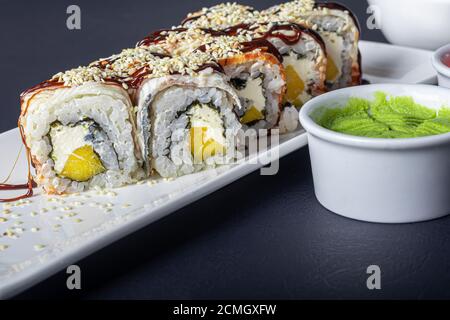 Sushi setzt Uramaki, California, Philadelphia, auf einen weißen Teller. In der Nähe Ingwer und Wasabi. Sojasauce in einer weißen Schüssel. Auf einem dunklen Hintergrund. Speicherplatz kopieren. Stockfoto