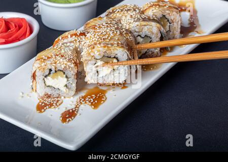 Sushi setzt Uramaki, California, Philadelphia, auf einen weißen Teller. In der Nähe Ingwer und Wasabi. Sojasauce in einer weißen Schüssel. Auf einem dunklen Hintergrund. Speicherplatz kopieren. Stockfoto