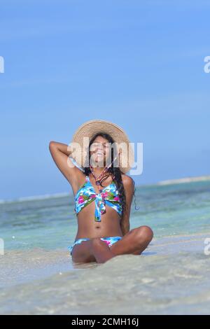 Hispanische Frau sitzt am Sandstrand und lacht mit geschlossenen Augen und Spritzwasser. Los Roques Venezuela Stockfoto